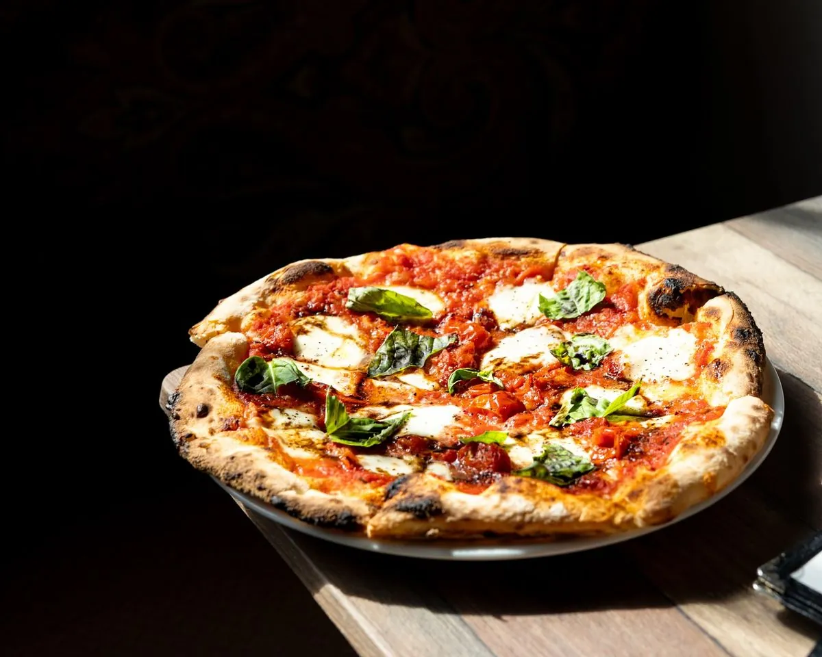 Una margherita appena sfornata, con il cornicione gonfio e bruciacchiato, su un tavolo di legno