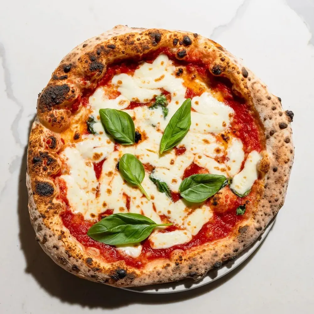 Una margherita vista dall'alto, con il cornicione bruciacchiato e le foglie di basilico, su un piano di marmo