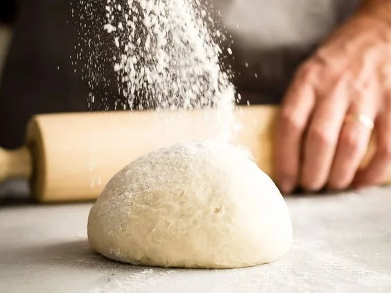 Una mano spolvera di farina una palla di impasto sul bancone, accanto al mattarello